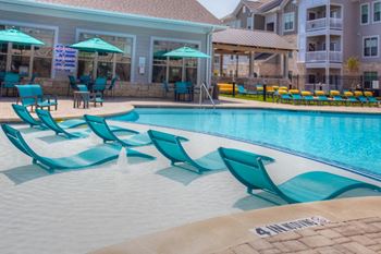 a swimming pool with blue chaise lounge chairs and umbrellas in front of a building
